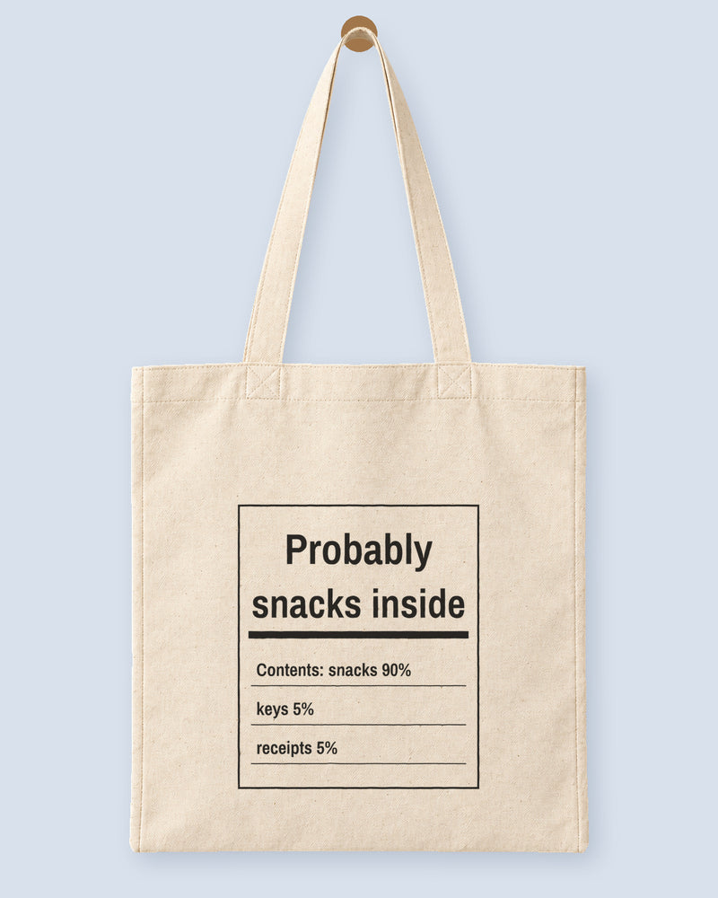 Natural canvas tote printed with “Probably snacks inside”, hanging on a wooden peg.