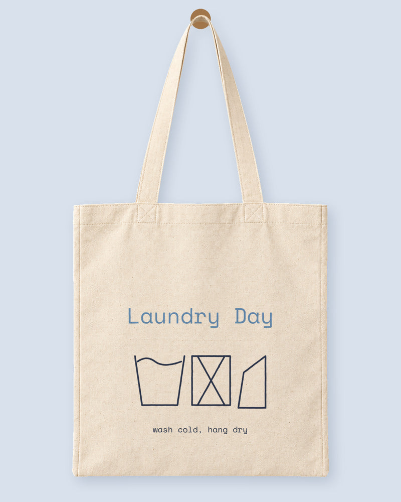 Natural canvas tote printed with “Laundry Day”, hanging on a wooden peg.