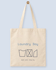 Natural canvas tote printed with “Laundry Day”, hanging on a wooden peg.