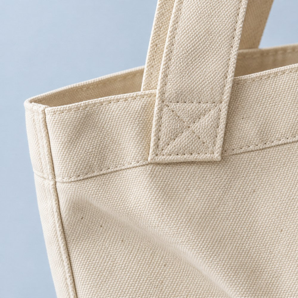 Illustrative close-up of natural cotton canvas weave and a stitched tote handle